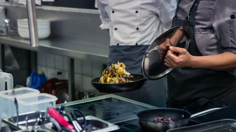 Zwei Personen kochen mit Pfanne am Herd