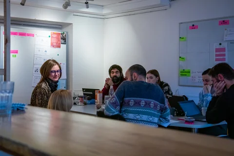 Eine vielfältige Gruppe von Kollegen versammelt sich an einem Tisch in einem hellen Büro, mit Whiteboards voller Notizen im Hintergrund.