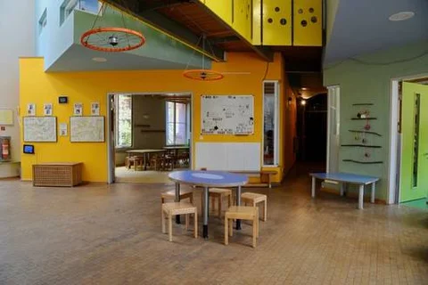 Moderner, farbenfroher Innenraum einer Schule oder Kita mit gelben und grünen Wänden, Tischen, Stühlen und Fahrradfelgen-Deko.