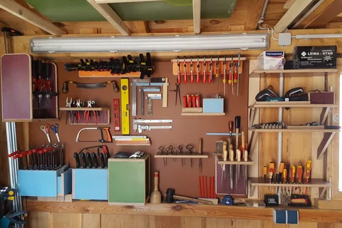 Eine saubere Werkstattwand voller akribisch organisierter Handwerkzeuge, darunter Zwingen, Meißel, Schraubendreher und Sägen.
