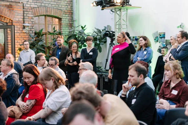 Eine Zuschauer*innengruppe. Eine Frau spricht. 