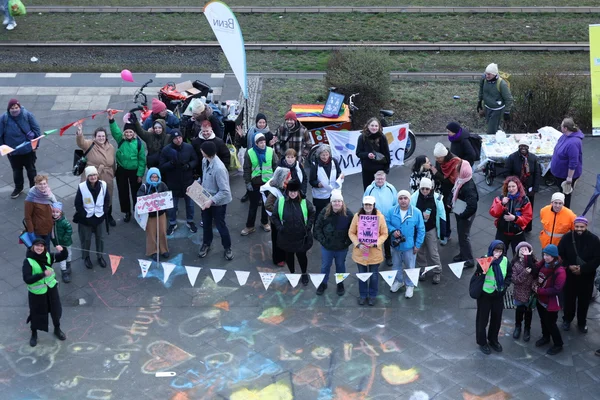 Vielfältige Menschengruppe draußen versammelt, hält Schilder wie 'FIGHT RACISM', steht auf bunten Kreidezeichnungen.