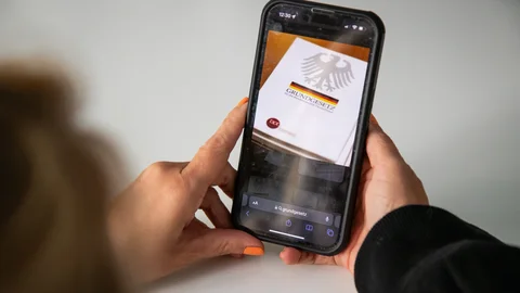 Smartphone zeigt das deutsche Grundgesetz mit Bundesadler, gehalten von Händen.
