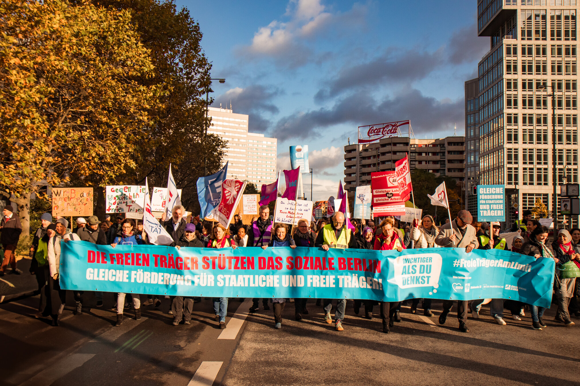 Demonstranten in Berlin halten ein blaues Banner mit der Aufschrift 'Die freien Träger stützen das soziale Berlin - Gleiche Förderung für staatliche und freie Träger!'.