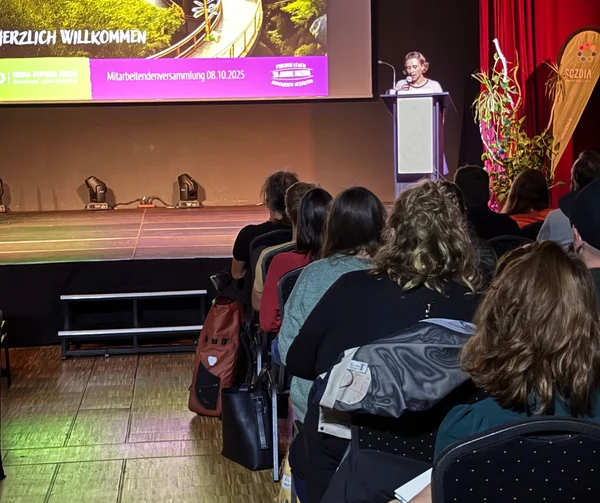 Eine Frau steht auf einer Bühne vor einem Mikrofon und spricht.