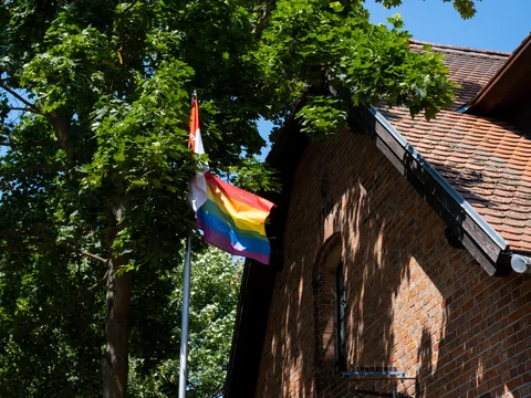 Eine Pride Flagge weht vor der Eisschmiede Uckermark vor blauem Himmel.