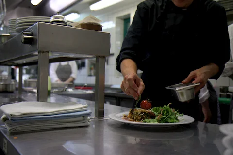 Koch in schwarzer Kleidung richtet Teller mit Salat und Tomate in einer professionellen Restaurantküche an
