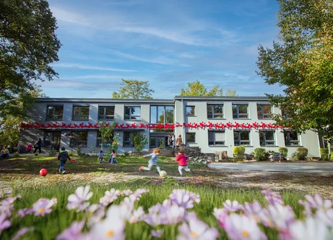 Die Kita Spreeknirpse im Sommer. EIn helles Haus umgeben von Grün.