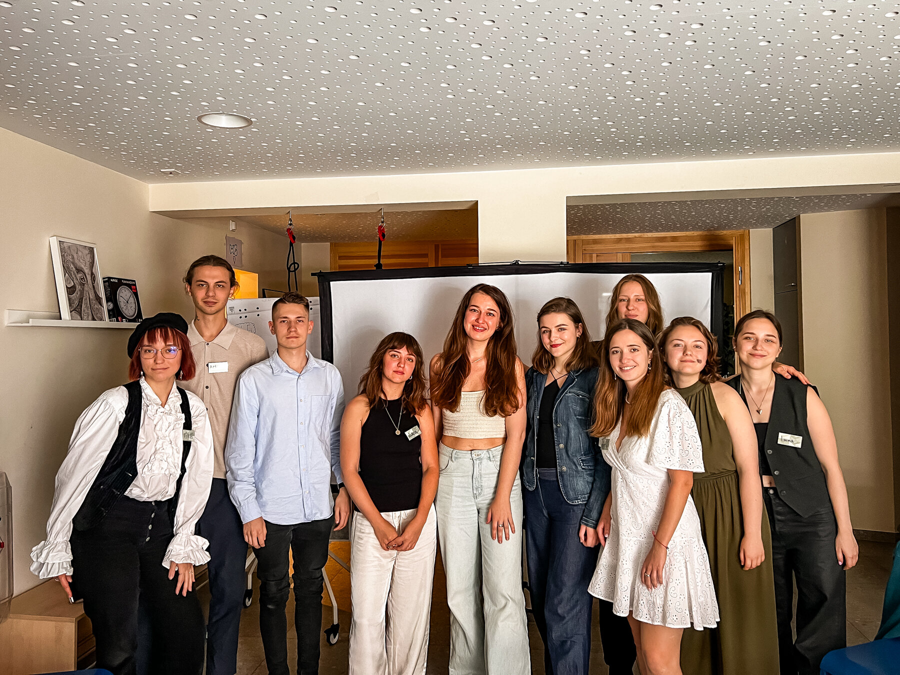 Elf junge Leute, eine Mischung aus Männern und Frauen, stehen drinnen und lächeln für ein Gruppenfoto.