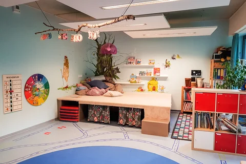 Ein farbenfroher Kinderraum mit gemütlicher Leseecke, dekorierten Wänden, einem Straßenmusterboden und Büchern und Spielzeug.