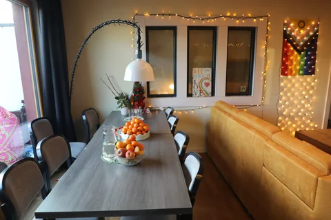 Ein gemütliches Wohnzimmer mit Esstisch. An der Wand hängt eine PrideFlagge sowie Lichterketten.