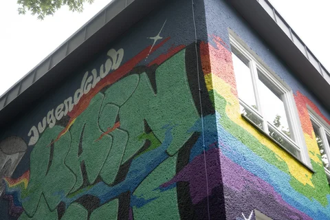 Bunte Graffiti mit dem Wort 'Jugendclub' an der Ecke eines mehrstöckigen Hauses mit zwei Fenstern