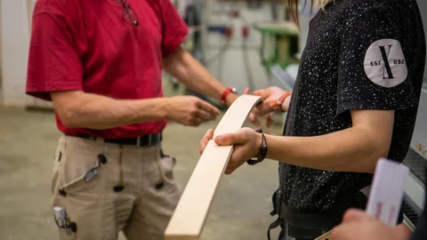 Zwei Personen in einer Werkstatt begutachten ein gebogenes Holzstück.