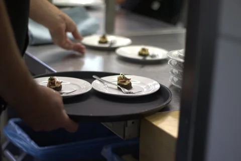 Hand hält Tablett mit mehreren kleinen Tellern, auf denen jeweils eine kleine Portion Essen angerichtet ist