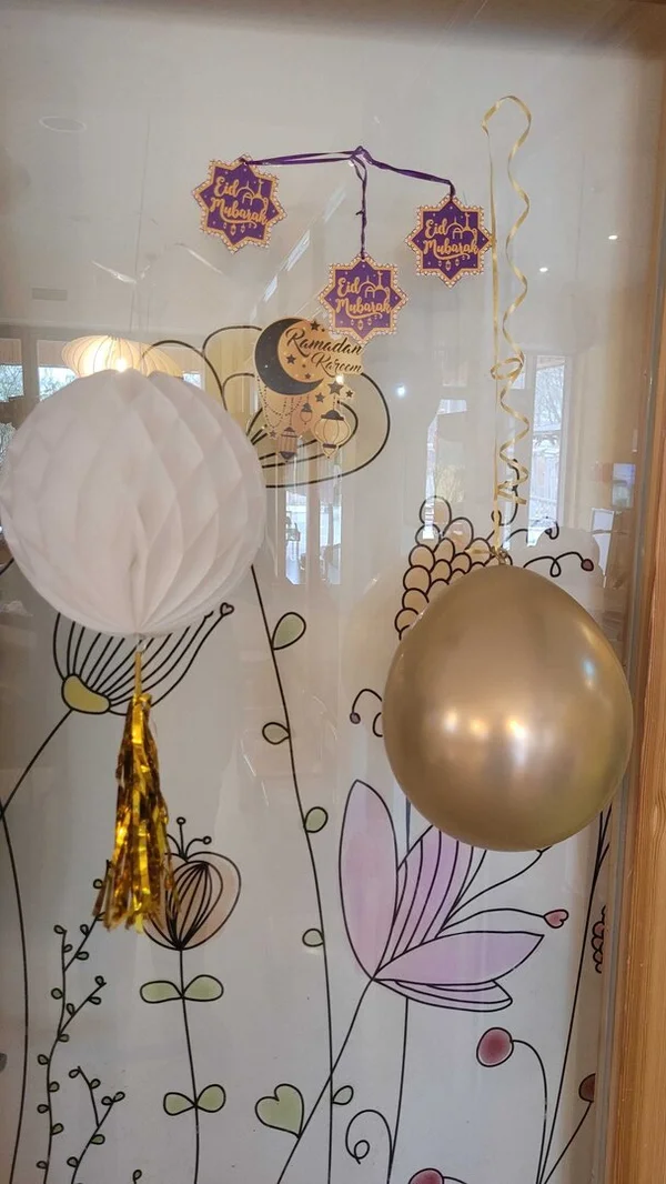 Glasfenster dekoriert mit Eid Mubarak Mobile, Ramadan Kareem Aufkleber, weißer Wabenlaterne und Goldballon.