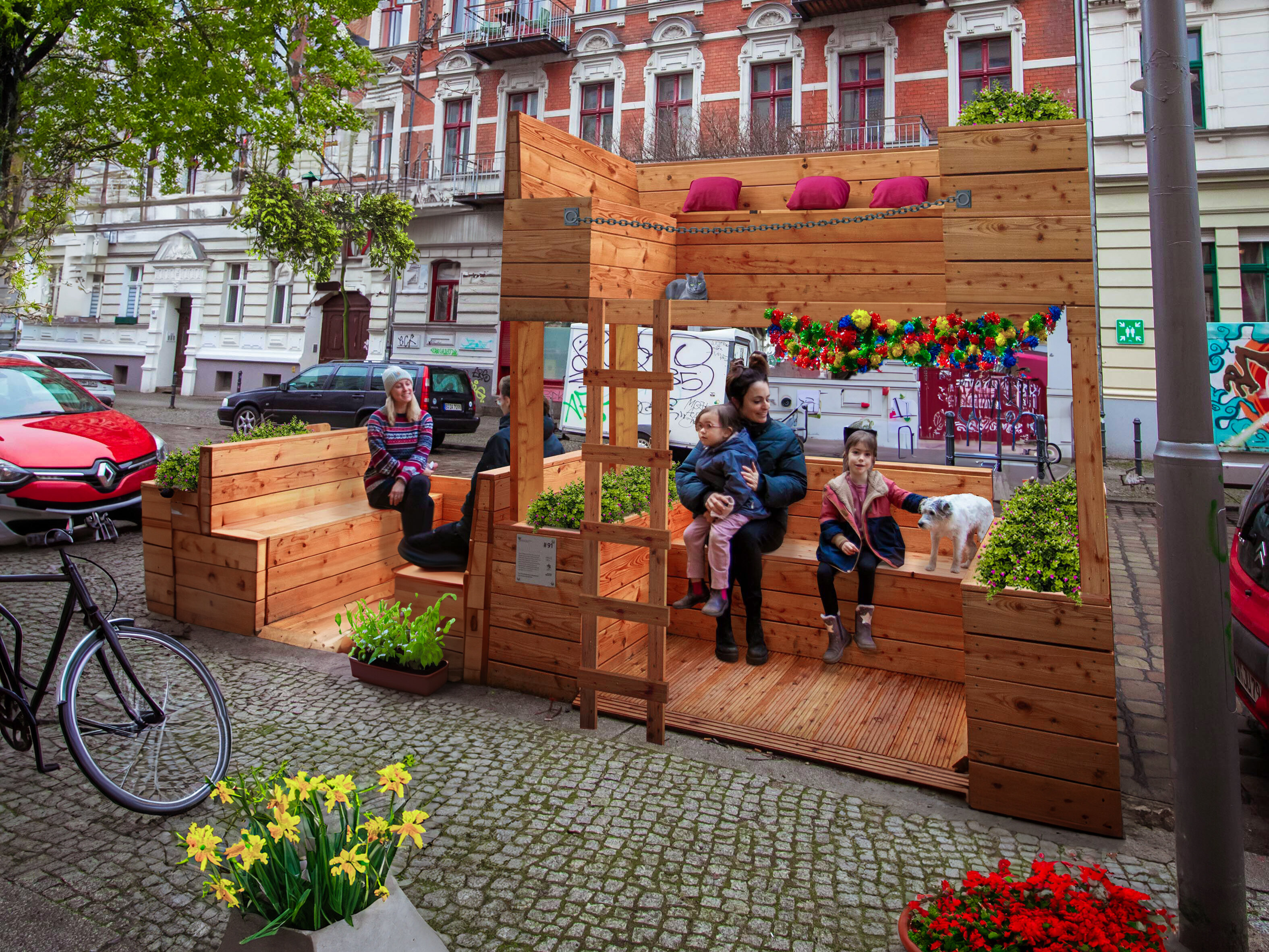 Holz-Parklet auf einer Kopfsteinpflasterstraße mit sitzenden Frauen, Kindern und einem Hund, umgeben von Pflanzen und Deko.