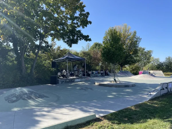 Eine Band spielt unter einem Zelt in einem mit Graffiti versehenen Skatepark an einem sonnigen Tag, umgeben von Bäumen.