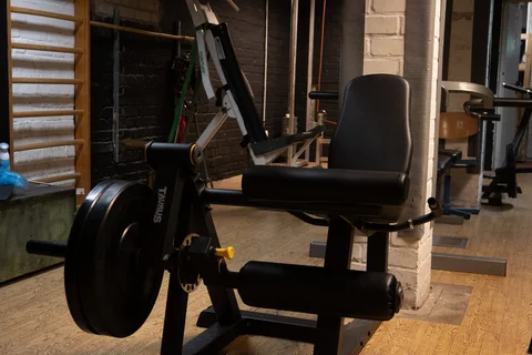Beinpresse mit Sitz und gepolsterten Rollen in einem Fitnessraum mit Spiegel und Holzlattenwand