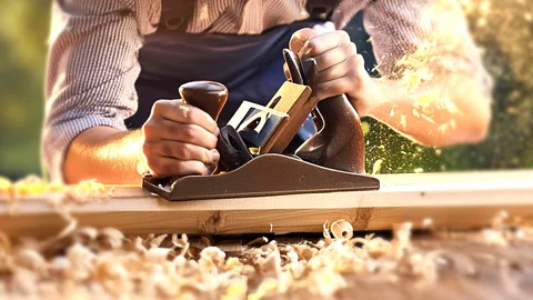 Hände halten einen Hobel und hobeln ein Brett