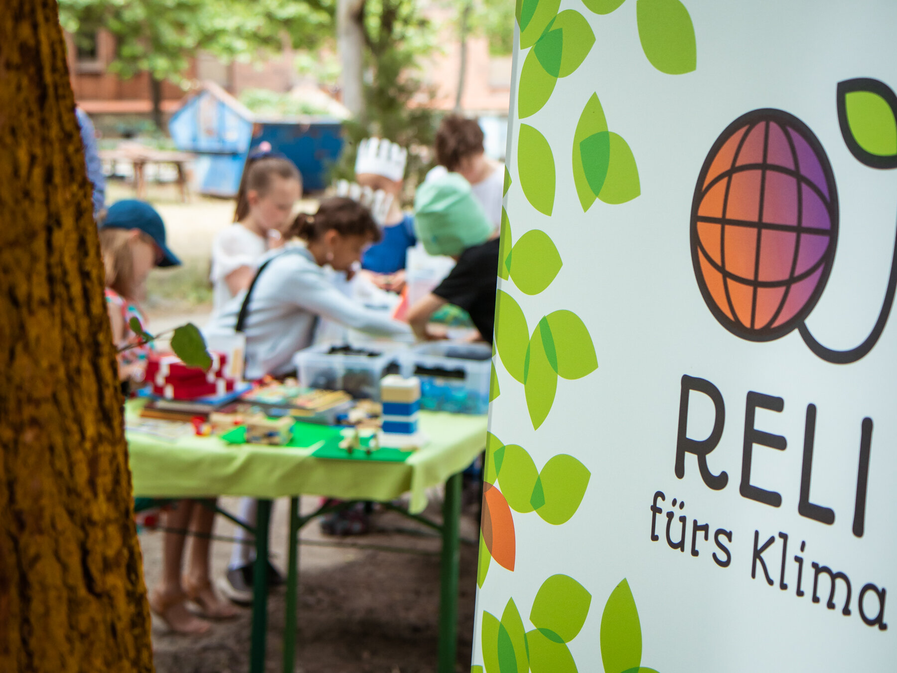 Ein Banner mit der Aufschrift "Reli fürs Klima" steht vor Kindern, die Pflanzen pikieren