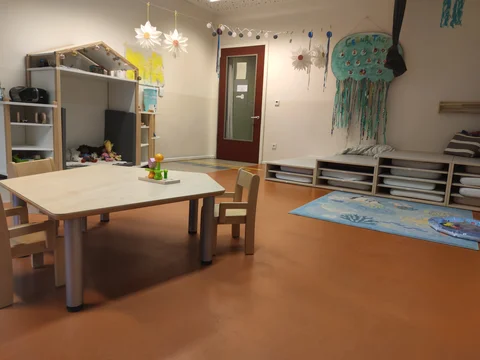 Ein farbenfrohes und gut ausgestattetes Kinderspielzimmer mit Tisch, Stühlen, Stauraum, Spielbereich und Dekorationen.