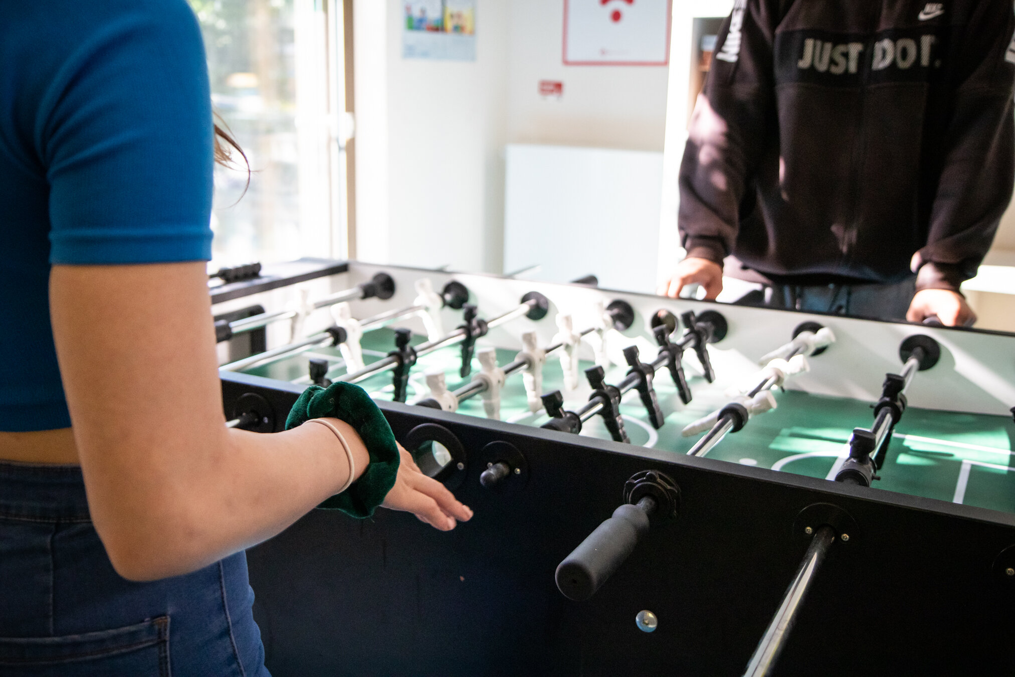 Zwei Personen spielen Tischfußball, eine in Blau, eine in Schwarz, konzentriert auf das Spiel.