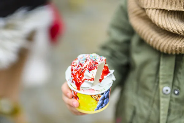 Ein Kind hat einen Eisbecher mit bunten Streuseln in der Hand. 