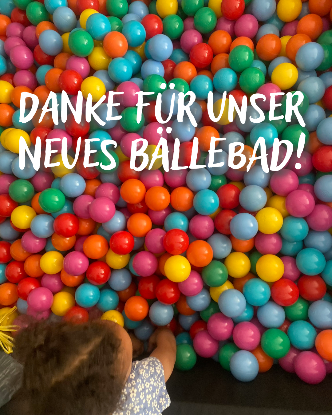 Buntes Bällebad mit vielen farbigen Plastikbällen und einem kleinen Kind, das von oben hineingreift.